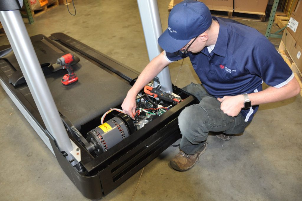 A Heartline Fitness technician repairs a treadmill during a Preventive Maintenance session.